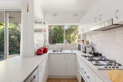 a white kitchen with a stove and a sink at Lovely Harbourside 1-Bed Close To Sydney Landmarks in Sydney