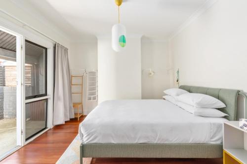 a white bedroom with a bed and a window at Stylish 2-Bed Cottage in Trendy Erskineville in Sydney