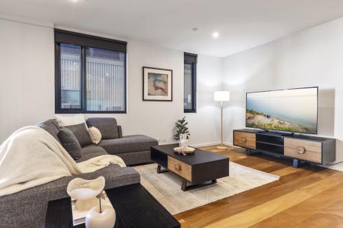 a living room with a couch and a flat screen tv at Oceanfront 2-Bed With Balcony & Study Nook in Geelong
