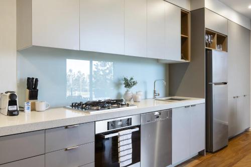 Una cocina con gabinetes blancos y un horno de estufa. en Oceanfront 2-Bed With Balcony & Study Nook, en Geelong