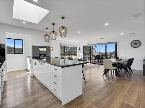 a kitchen with white cabinets and a dining room with a table at Chic 4-Bed with 3 Living Areas & Alfresco Dining in Malua Bay