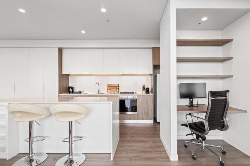 a kitchen with white cabinets and bar stools at Luxe 2-Bed: Modern Interiors Balcony & BBQ Area in Sydney