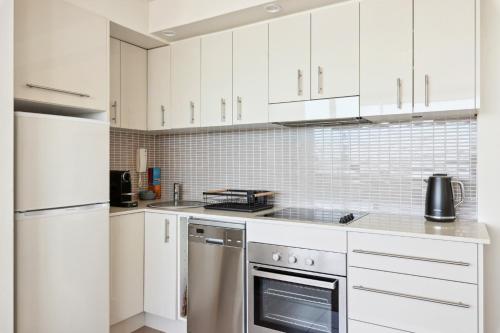a kitchen with white cabinets and stainless steel appliances at Wake Up to the Ocean: 1-Bed with Pool & Views in Sydney