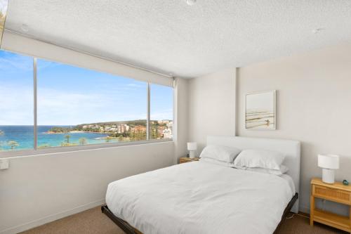 a bedroom with a large white bed and a large window at Wake Up to the Ocean: 1-Bed with Pool & Views in Sydney