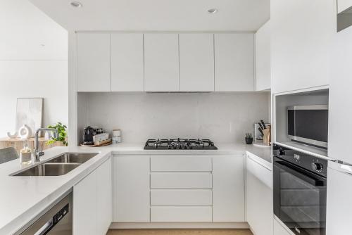 une cuisine blanche avec un évier et une cuisinière dans l'établissement Lovely 3-Bed with Alfresco Dining by Attractions, à Kiama