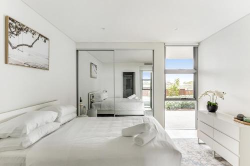 a white bedroom with two beds and a mirror at Lovely 3-Bed with Alfresco Dining by Attractions in Kiama