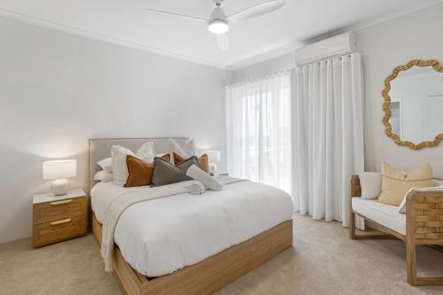 ein weißes Schlafzimmer mit einem großen Bett und einem Stuhl in der Unterkunft Stylish 3-Bed Apartment in Coastal Redcliffe in Redcliffe