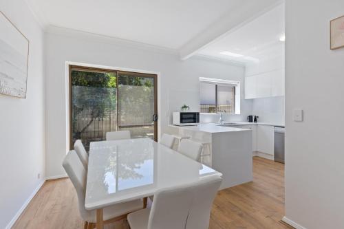une cuisine et une salle à manger avec une table et des chaises blanches dans l'établissement Elegant 3-Bed Home Steps from Sunny Glenelg Beach, à Glenelg