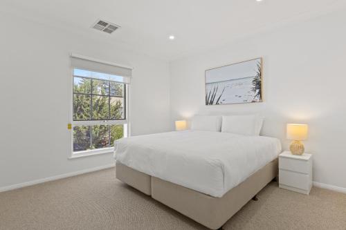 une chambre blanche avec un lit et deux fenêtres dans l'établissement Elegant 3-Bed Home Steps from Sunny Glenelg Beach, à Glenelg