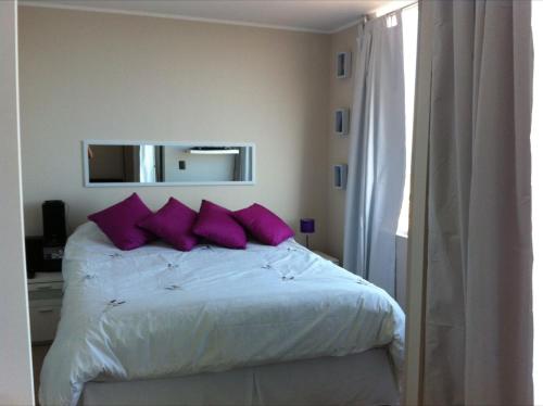 1 dormitorio con cama con almohadas moradas y espejo en Barcelo Suites Viña del Mar, en Viña del Mar