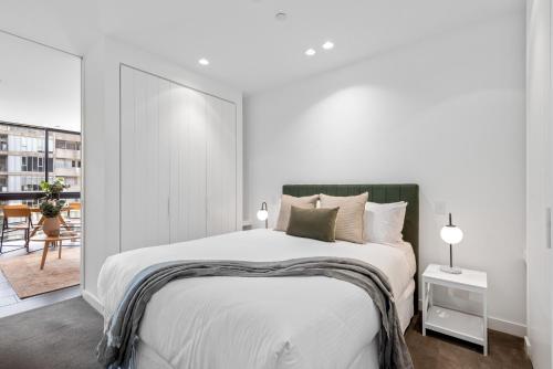 a white bedroom with a large bed and a balcony at Chic City Escape with Pool, Gym & Parking in Melbourne