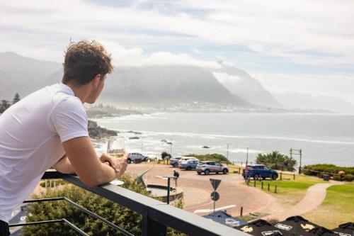 Ein Mann steht auf einem Balkon mit Meerblick in der Unterkunft Oceanfront Duplex Apartments, Hermanus Waterfront in Hermanus