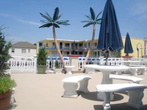 a group of tables and chairs with an umbrella and palm trees at Casa Del Sol Motel in Wildwood