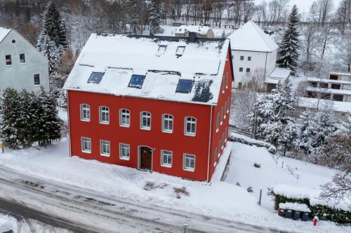 un bâtiment rouge recouvert de neige dans l'établissement Erzgebirge Apartments Sehmatal, à Sehma
