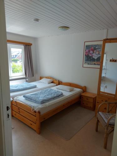 a bedroom with two beds and a chair and a window at Haus Klaarstrand in Wenningstedt