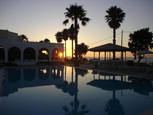 a sunset over a pool with palm trees and a building at Andromeda Hotel Apartments in Kos Town