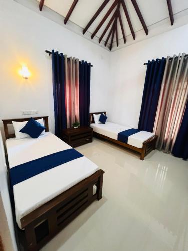 two beds in a room with blue curtains at Yala Mangora Inn in Tissamaharama