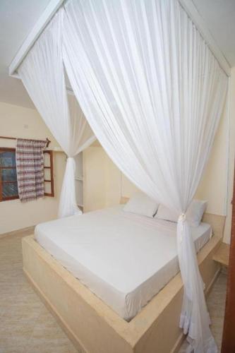 a white bed with white curtains in a bedroom at GK Palm Resort Watamu in Watamu