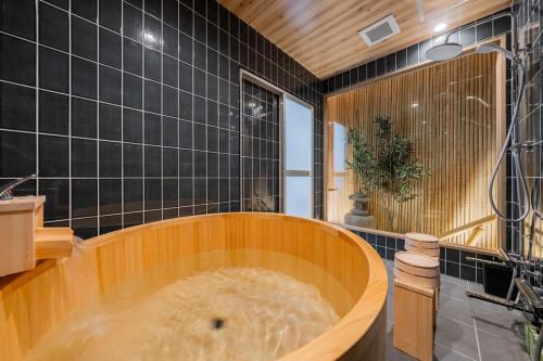 a large wooden tub in a bathroom with black tiles at 蝶 プレイルーム家族で楽しめるお部屋 手作りの和風のお部屋で疲れを癒す 11台のベッド 22名利用 in Osaka