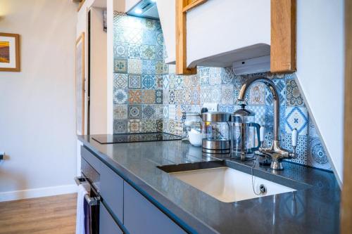 una cucina con lavandino e piastrelle blu sul muro di The Old Smithy - 2 Bedroom Cottage - Reynoldston a Reynoldston