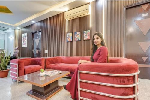 a woman sitting on a red couch in a living room at Via Next Home - Nr IMT Chowk Manesar in Gurgaon