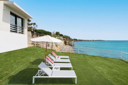a row of lounge chairs with an umbrella and the ocean at Villa Hermes in Noto Marina