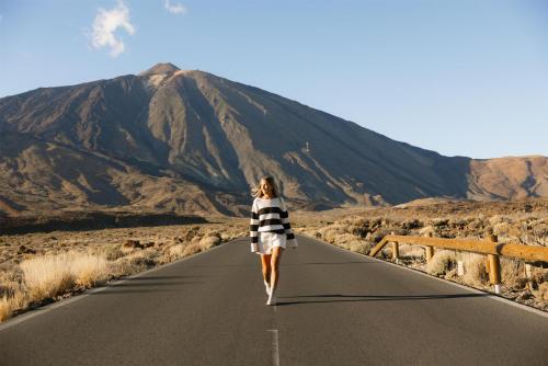 Eine Frau, die eine Straße entlang geht, mit einem Berg im Hintergrund in der Unterkunft Radisson Resort & Residences Tenerife - Adults Only in Puerto de la Cruz