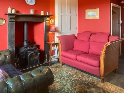 a red couch in a living room with a fireplace at Downhouse Cottage in Delabole