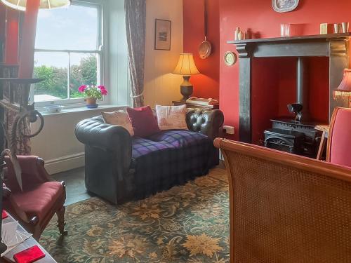 a living room with a leather couch and a fireplace at Downhouse Cottage in Delabole