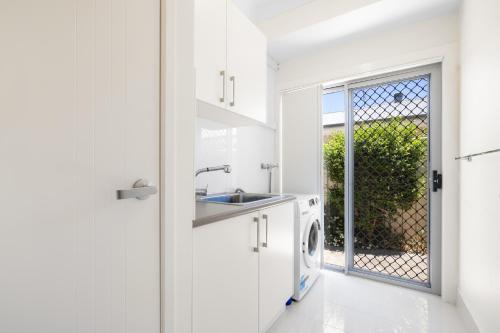 a white kitchen with a sink and a washing machine at Sea La Vie in Arakoon