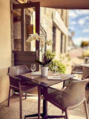 a wooden table with two chairs and a vase with flowers at Aux 13 Arches-Logis Hôtel Restaurant in Portbail