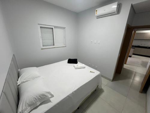 a white bedroom with a bed with a black bag on it at Apartamento com jardim e ar condicionado na sala e quartos na Av Blumenau in Sorriso