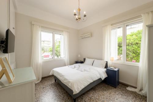 ein weißes Schlafzimmer mit einem Bett und zwei Fenstern in der Unterkunft Bright & Cozy House near Beach in Athen