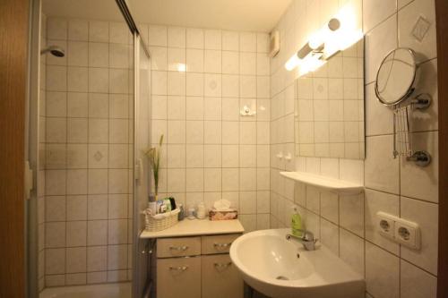 La salle de bains est pourvue de carrelage blanc, d'un lavabo et d'une douche. dans l'établissement Fewo Silberglanz, à Sehmatal