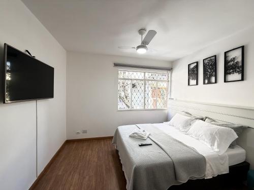 a white bedroom with a bed and a flat screen tv at Apartamento em Belo Horizonte in Belo Horizonte