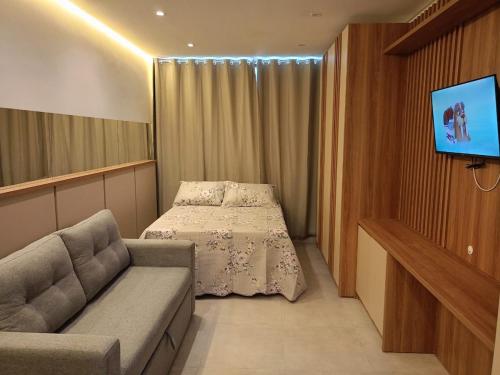 a room with a bed and a couch and a tv at Flat has rooftop with barbecue and sea view in Tamandaré