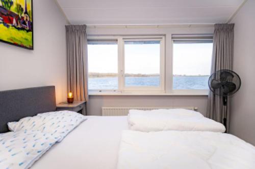 - une chambre avec un lit blanc et 2 fenêtres dans l'établissement Watervilla Den Oever VP066, à Wieringerwerf
