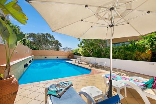 an umbrella and chairs next to a swimming pool at Santorini Twin Waters in Mudjimba