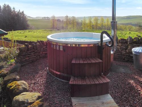 einen Whirlpool in einem Garten mit einer Steinmauer in der Unterkunft Grooms Cottage in Elsdon