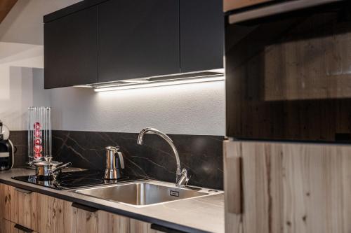 una cocina con fregadero y armarios negros en Suite Illuminata con piccolo centro wellness, en Commezzadura