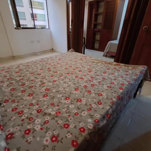 ein Bett mit einer Decke mit roten Blumen drauf in der Unterkunft Quédate En El Punto Más Central De Manizales in Manizales