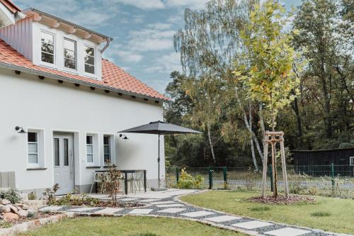 une maison blanche avec une table et un parasol dans l'établissement Spreewaldhaus Am Landgut Der Stall, à Markische Heide