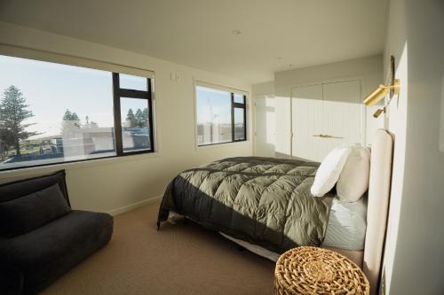 a bedroom with a bed and a couch and windows at Belle Mer Beachfront Apartments in Mount Maunganui