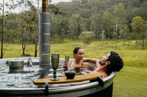 a man and woman in a hot tub with drinks at The Lookout - a Huch experience in Wollombi