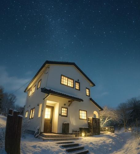 a large white house in the snow at night at 八ヶ岳南麓の貸切宿 駅徒歩5分 スキー場まで車で15分 テラスでバーベキュー 広い庭と遊具付き 富士山と南アルプスを望む宿 in Nagasawa