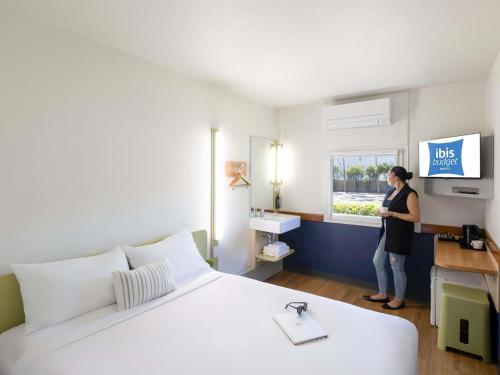 a woman standing in a hotel room with a bed at ibis Budget Wentworthville in Wentworthville