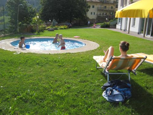 a woman sitting in a chair in a yard with children in a pool at Residence Wiesenheim in Trodena