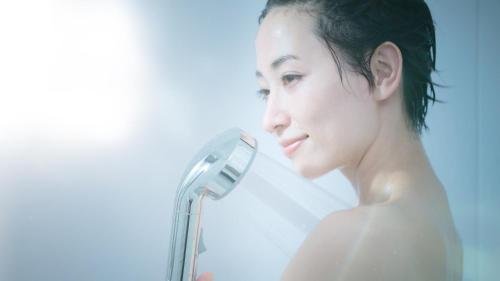 a woman in a shower holding a shower head at Hotel Yamagata Hills Ekimae Odori in Yamagata