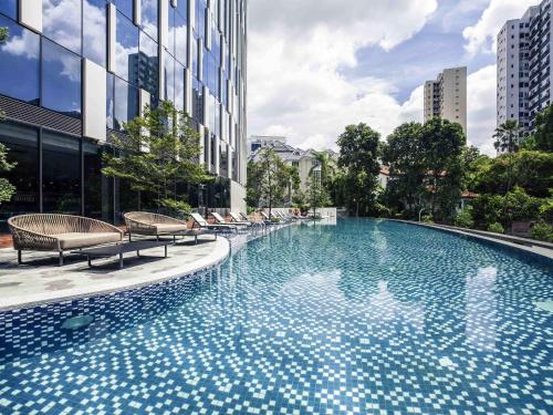 ein großes Schwimmbad mit Stühlen und einem Gebäude in der Unterkunft Mercure Singapore On Stevens in Singapur