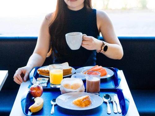 uma mulher sentada numa mesa com uma bandeja de comida para o pequeno-almoço em ibis budget Sao Jose do Rio Preto em Sao Jose do Rio Preto